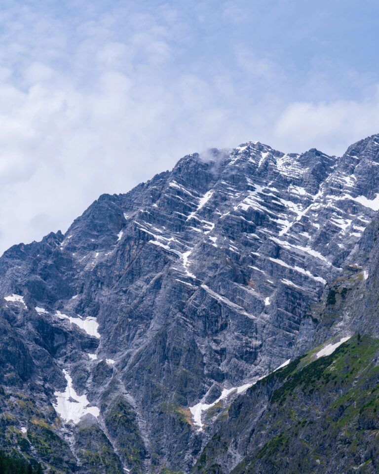 Majestic snow-dusted mountain peaks with a dramatic rocky terrain and partly cloudy sky.